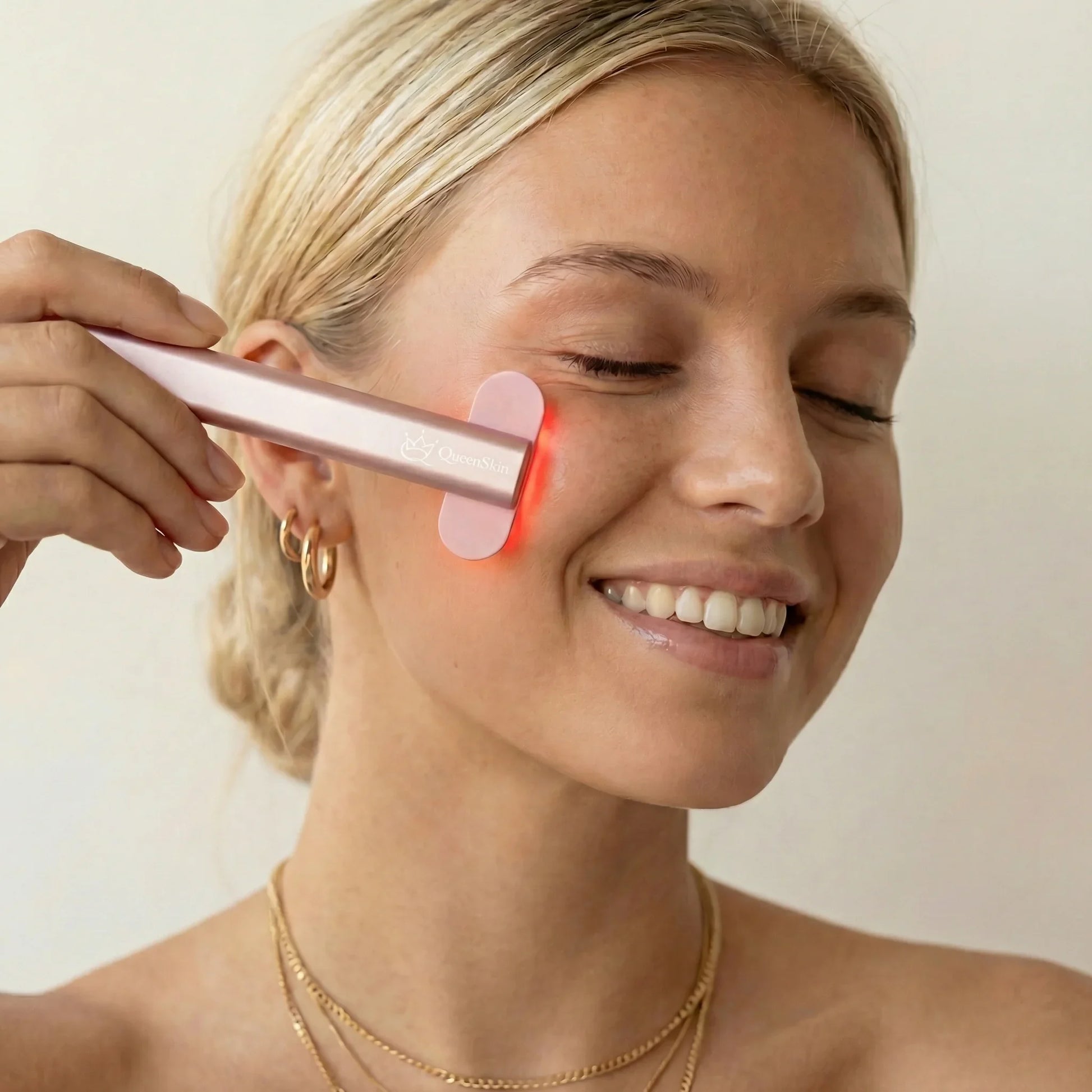 Woman using QueenSkin microcurrent device on cheek for skincare treatment