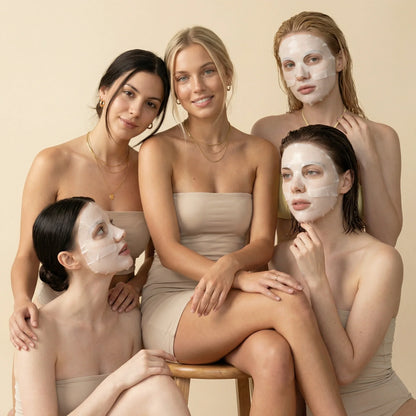 Group of women in neutral dresses, some wearing QueenSkin hydrogel face masks, studio setting